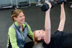 One woman lifting weights and another one spotting her